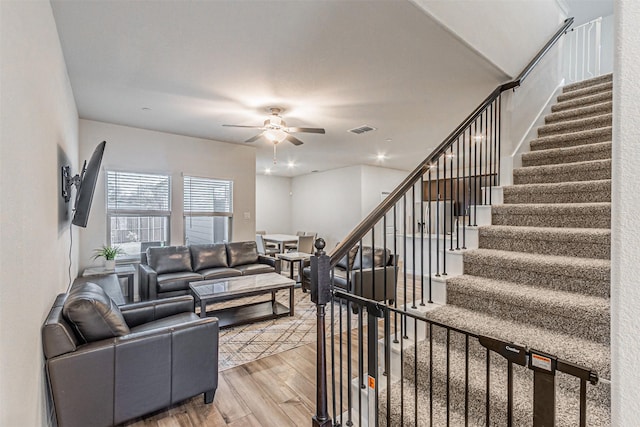 living area featuring stairway, a ceiling fan, visible vents, and light wood-type flooring