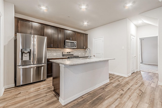 kitchen with tasteful backsplash, dark brown cabinets, a center island with sink, light wood-style flooring, and stainless steel appliances