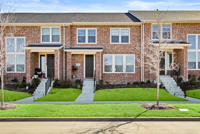 view of property featuring brick siding, roof with shingles, and a front yard