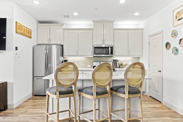 kitchen featuring light wood-style flooring, a breakfast bar area, tasteful backsplash, and appliances with stainless steel finishes