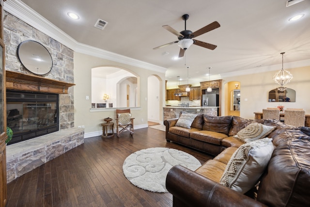 living area featuring visible vents, ornamental molding, dark wood-style floors, arched walkways, and a stone fireplace