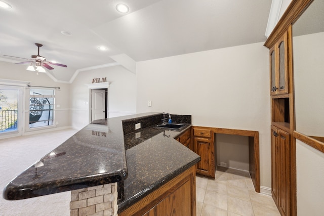 kitchen with ceiling fan, lofted ceiling, dark stone countertops, brown cabinetry, and a sink