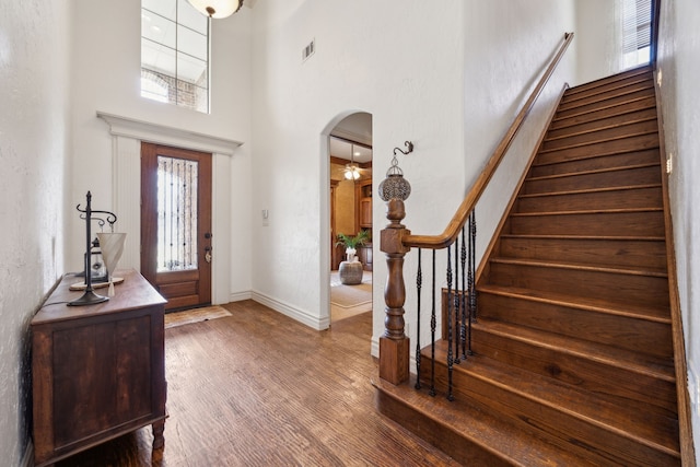 foyer featuring wood finished floors, arched walkways, a high ceiling, baseboards, and stairs