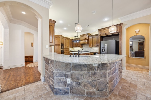 kitchen with ornamental molding, stone tile floors, arched walkways, stainless steel fridge, and a sink