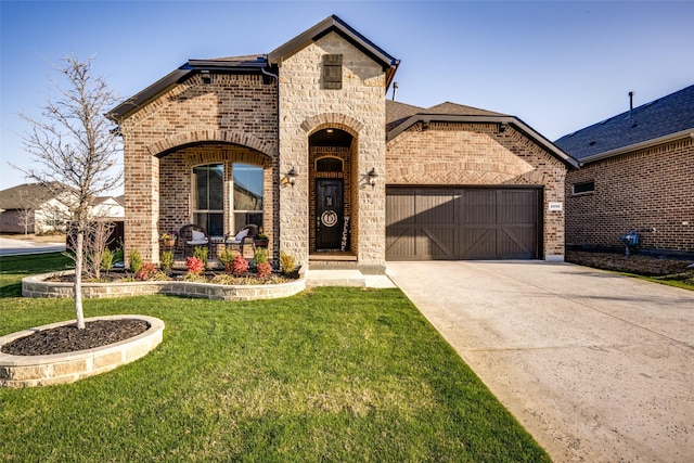 french country home featuring brick siding, an attached garage, concrete driveway, and a front lawn