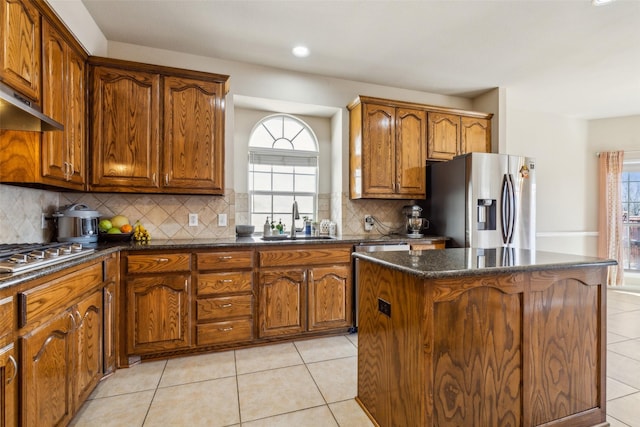 kitchen featuring a kitchen island, light tile patterned floors, brown cabinetry, stainless steel appliances, and a sink