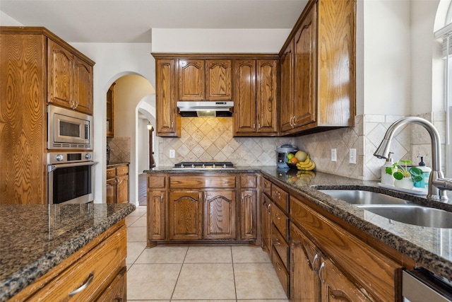 kitchen featuring under cabinet range hood, dark stone counters, appliances with stainless steel finishes, and a sink