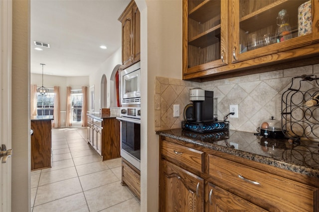 kitchen with light tile patterned floors, brown cabinets, arched walkways, and appliances with stainless steel finishes