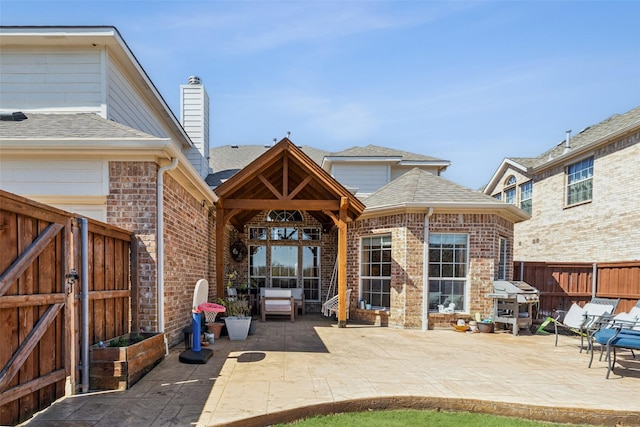 back of house featuring brick siding, a patio area, roof with shingles, and fence