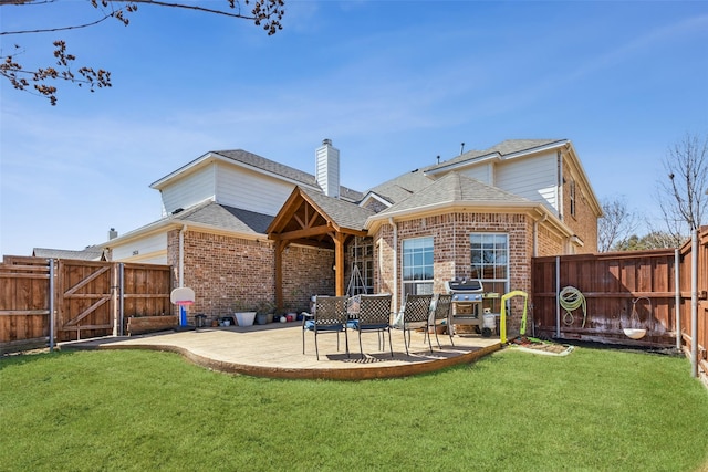 back of house with brick siding, a patio area, a lawn, and a fenced backyard