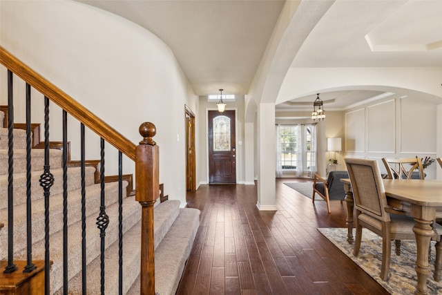 foyer with baseboards, arched walkways, dark wood-type flooring, and stairs