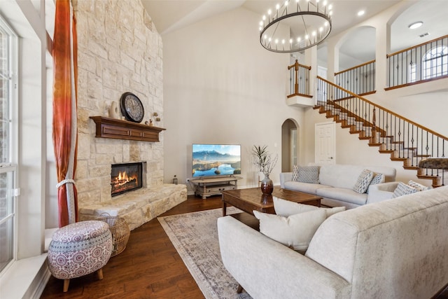 living area featuring a chandelier, a stone fireplace, arched walkways, dark wood-style floors, and high vaulted ceiling