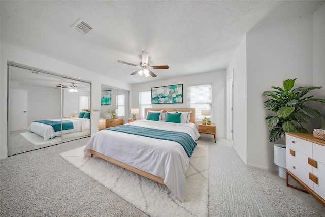 carpeted bedroom featuring a ceiling fan, visible vents, and a textured ceiling