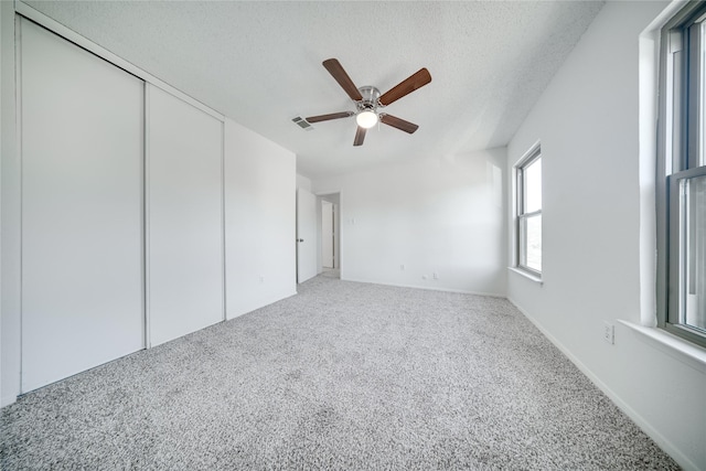 unfurnished bedroom featuring visible vents, a ceiling fan, a textured ceiling, a closet, and carpet flooring