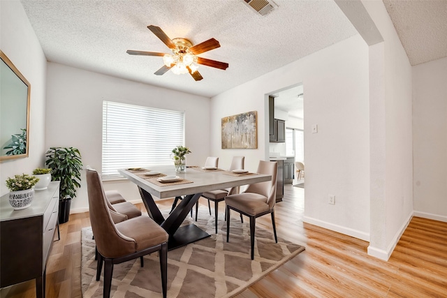 dining room with light wood-style flooring, visible vents, arched walkways, and a textured ceiling