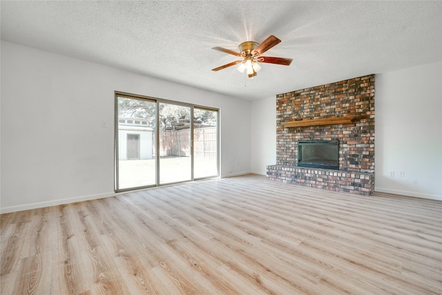 unfurnished living room featuring a textured ceiling, wood finished floors, a fireplace, baseboards, and ceiling fan