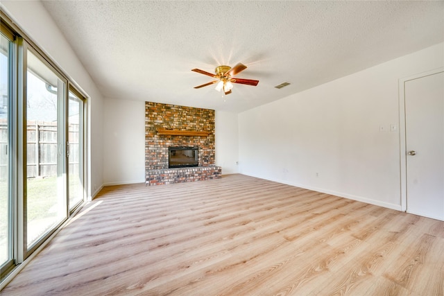 unfurnished living room with a fireplace, light wood-style floors, visible vents, and a textured ceiling