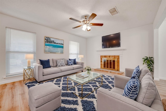 living area featuring visible vents, a fireplace, ceiling fan, and wood finished floors