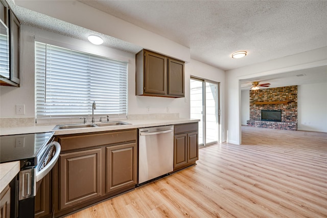 kitchen with a ceiling fan, a sink, stainless steel appliances, light wood-style floors, and a brick fireplace