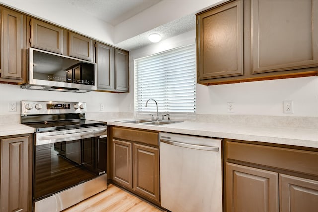 kitchen featuring light wood finished floors, light countertops, appliances with stainless steel finishes, a textured ceiling, and a sink