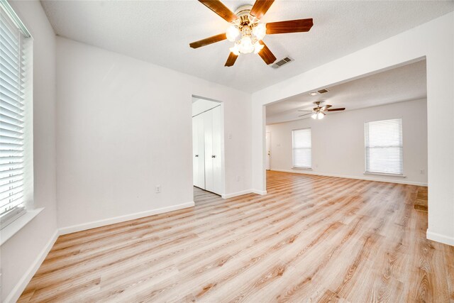 spare room featuring light wood-style flooring, baseboards, visible vents, and a textured ceiling