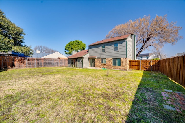 back of property with brick siding, a fenced backyard, a yard, and a gate