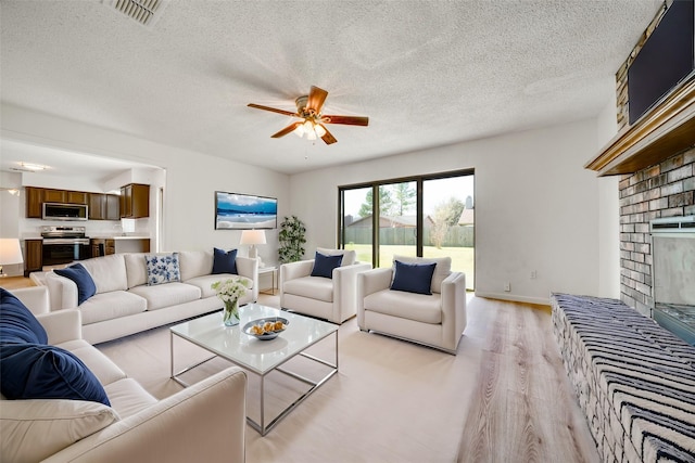 living room featuring visible vents, ceiling fan, light wood-style flooring, a fireplace, and a textured ceiling