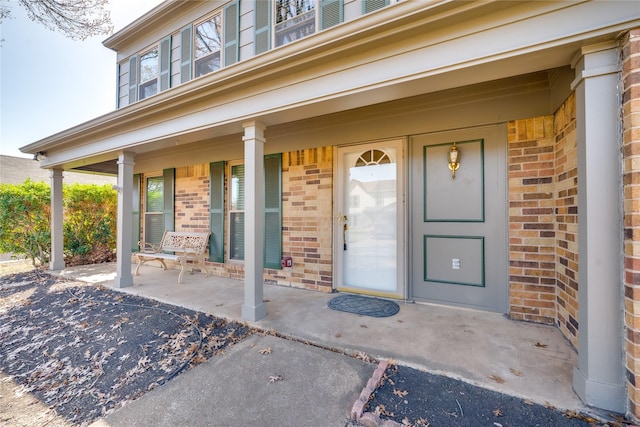 doorway to property featuring a porch and brick siding