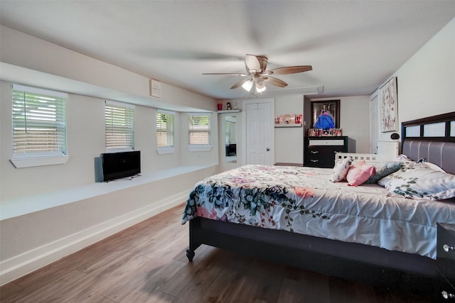 bedroom featuring ceiling fan, baseboards, multiple windows, and wood finished floors