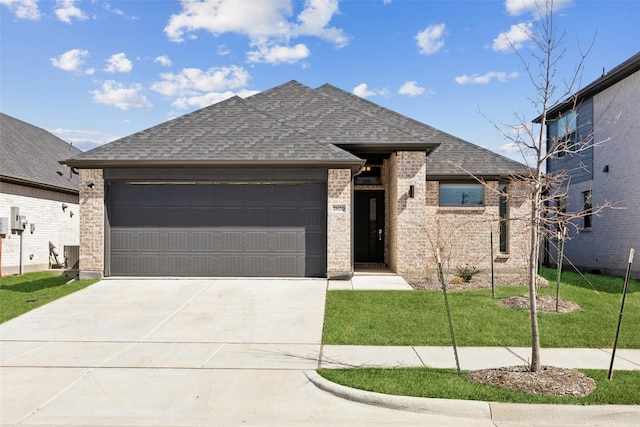 view of front of house featuring brick siding, a shingled roof, a front lawn, a garage, and driveway