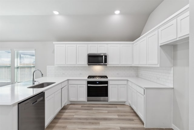 kitchen featuring a sink, stainless steel appliances, light wood-style floors, a peninsula, and vaulted ceiling