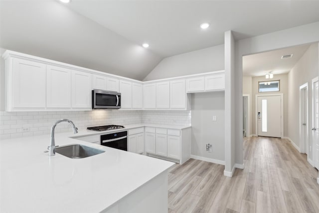 kitchen with lofted ceiling, a sink, appliances with stainless steel finishes, white cabinetry, and backsplash