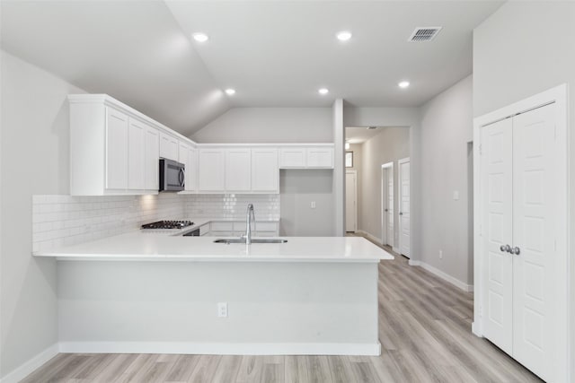 kitchen featuring a sink, stainless steel microwave, tasteful backsplash, a peninsula, and light countertops