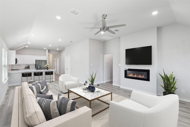 living room featuring visible vents, light wood-style flooring, recessed lighting, vaulted ceiling, and a glass covered fireplace