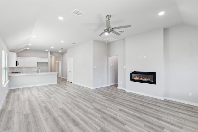 unfurnished living room featuring visible vents, light wood-style flooring, a glass covered fireplace, and vaulted ceiling