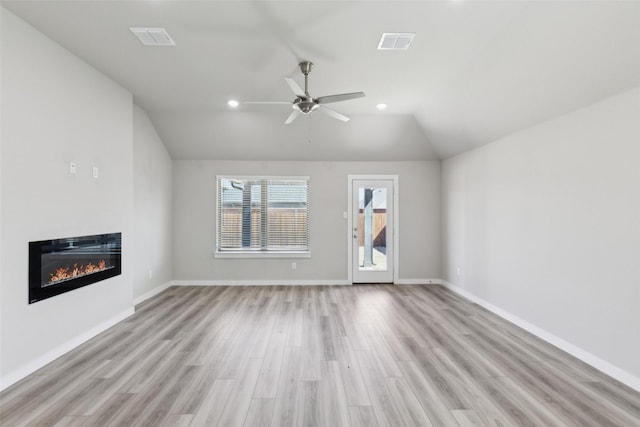 unfurnished living room featuring visible vents, lofted ceiling, ceiling fan, a glass covered fireplace, and light wood-type flooring