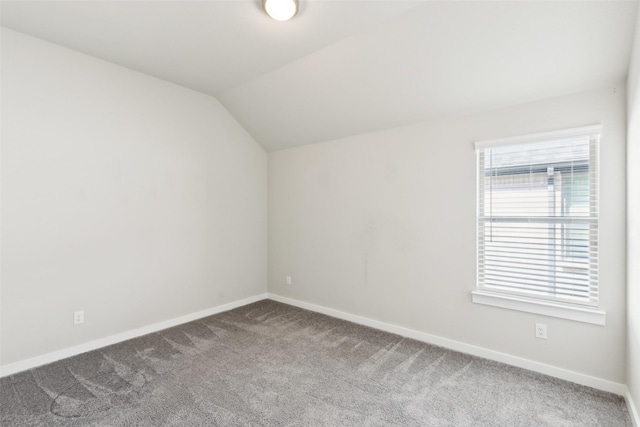 carpeted spare room featuring vaulted ceiling and baseboards