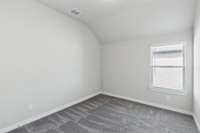 empty room featuring lofted ceiling, baseboards, visible vents, and dark colored carpet