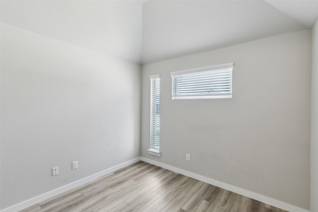 spare room featuring baseboards, light wood-style floors, and vaulted ceiling