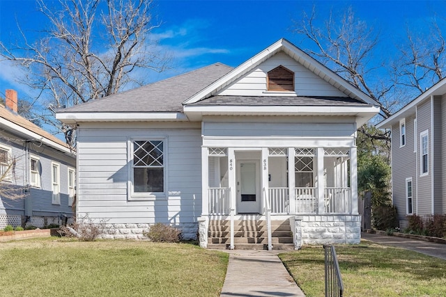 view of front of home with covered porch, a front yard, and a shingled roof