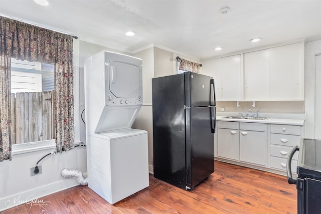 kitchen with a sink, freestanding refrigerator, light countertops, stacked washer / drying machine, and stove