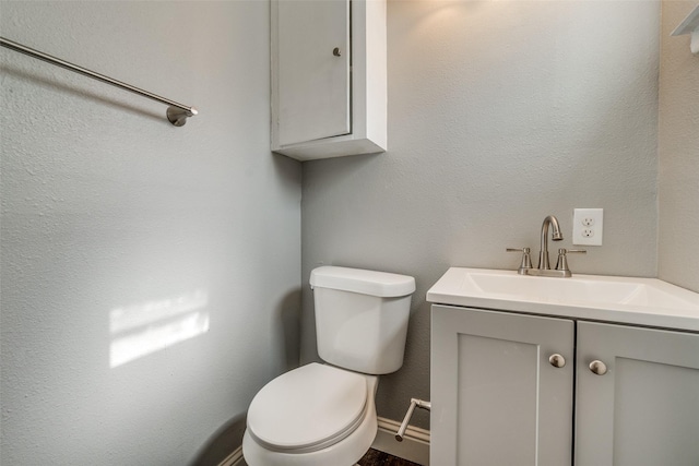 half bathroom with baseboards, toilet, and vanity