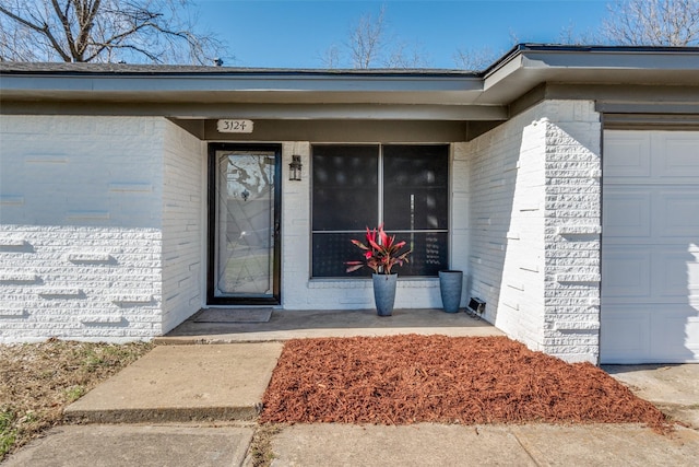 doorway to property with brick siding and a garage