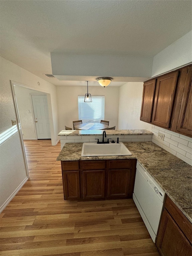 kitchen featuring a sink, a peninsula, white dishwasher, light wood finished floors, and decorative backsplash