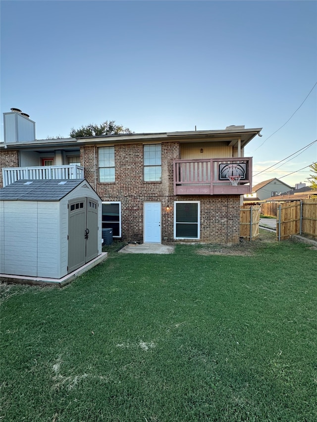 rear view of house with a storage unit, an outbuilding, a lawn, fence, and brick siding