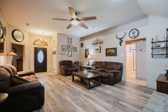 living room with light wood-type flooring, visible vents, ceiling fan with notable chandelier, and vaulted ceiling