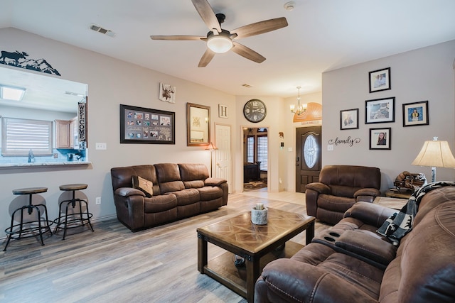 living area with light wood finished floors, visible vents, and ceiling fan with notable chandelier