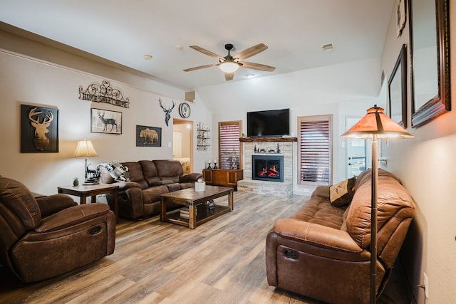 living room featuring visible vents, a ceiling fan, a stone fireplace, light wood finished floors, and vaulted ceiling