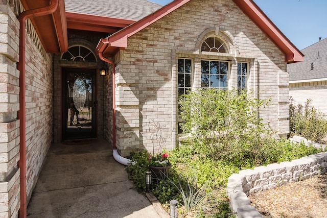 entrance to property featuring brick siding and a shingled roof