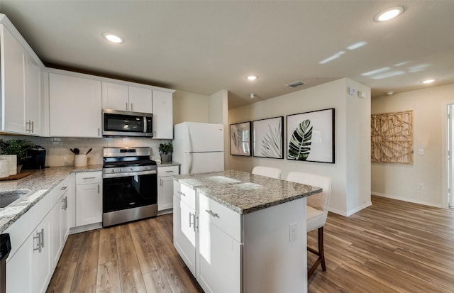 kitchen with light wood-type flooring, a kitchen bar, a center island, recessed lighting, and stainless steel appliances